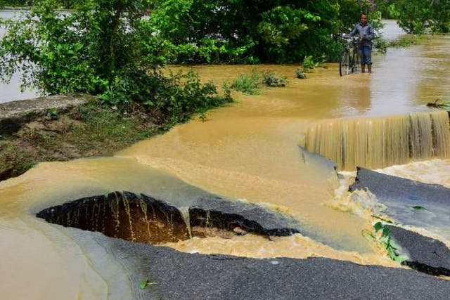 <p>A man pushes his bicycle along a damaged road due to flooding after heavy rains in Nagaon, Assam on 19 May</p>
