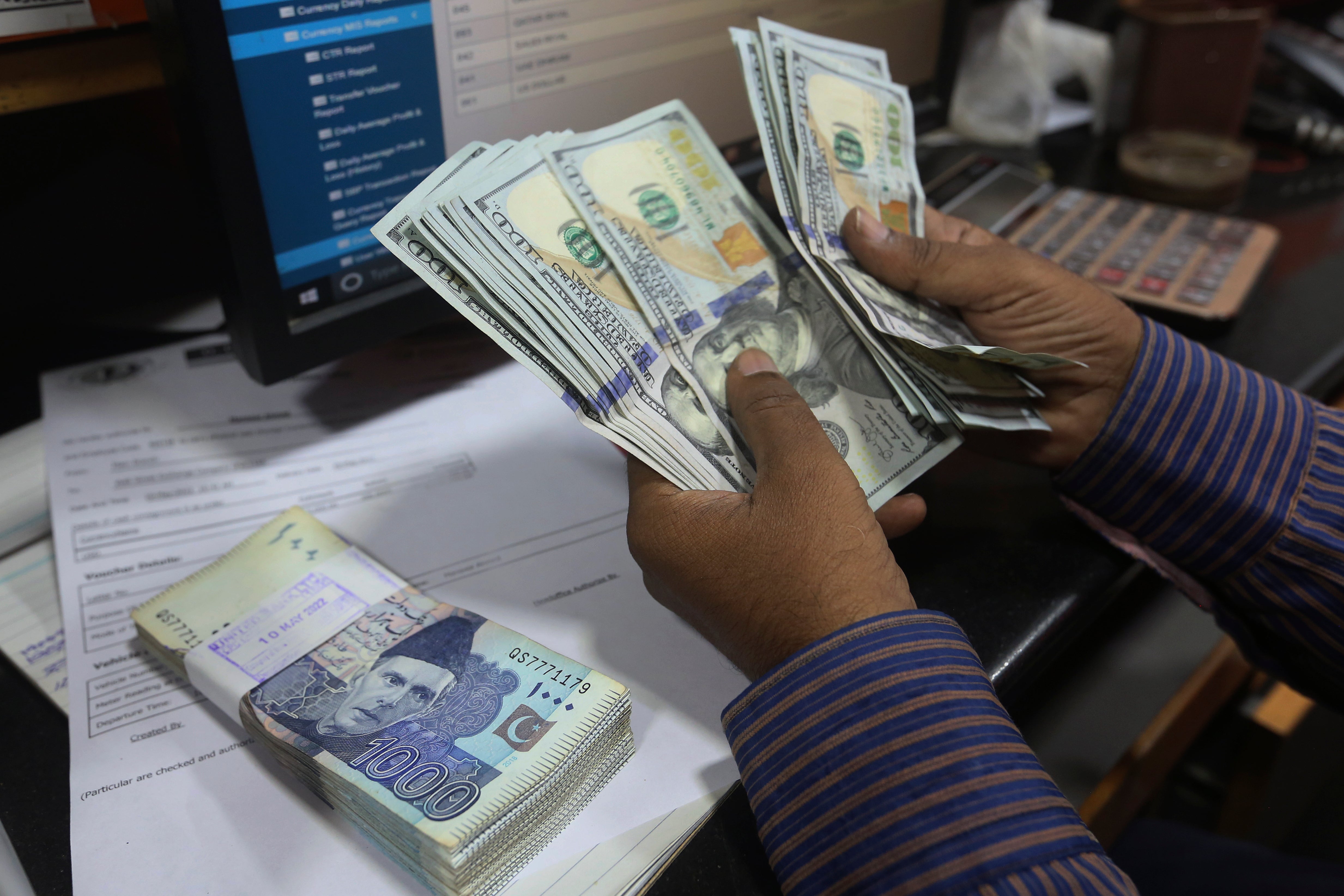 File. A Pakistani money trader counts US dollars for a customer at a currency exchange office, in Karachi, Pakistan, Thursday, 19 May 2022