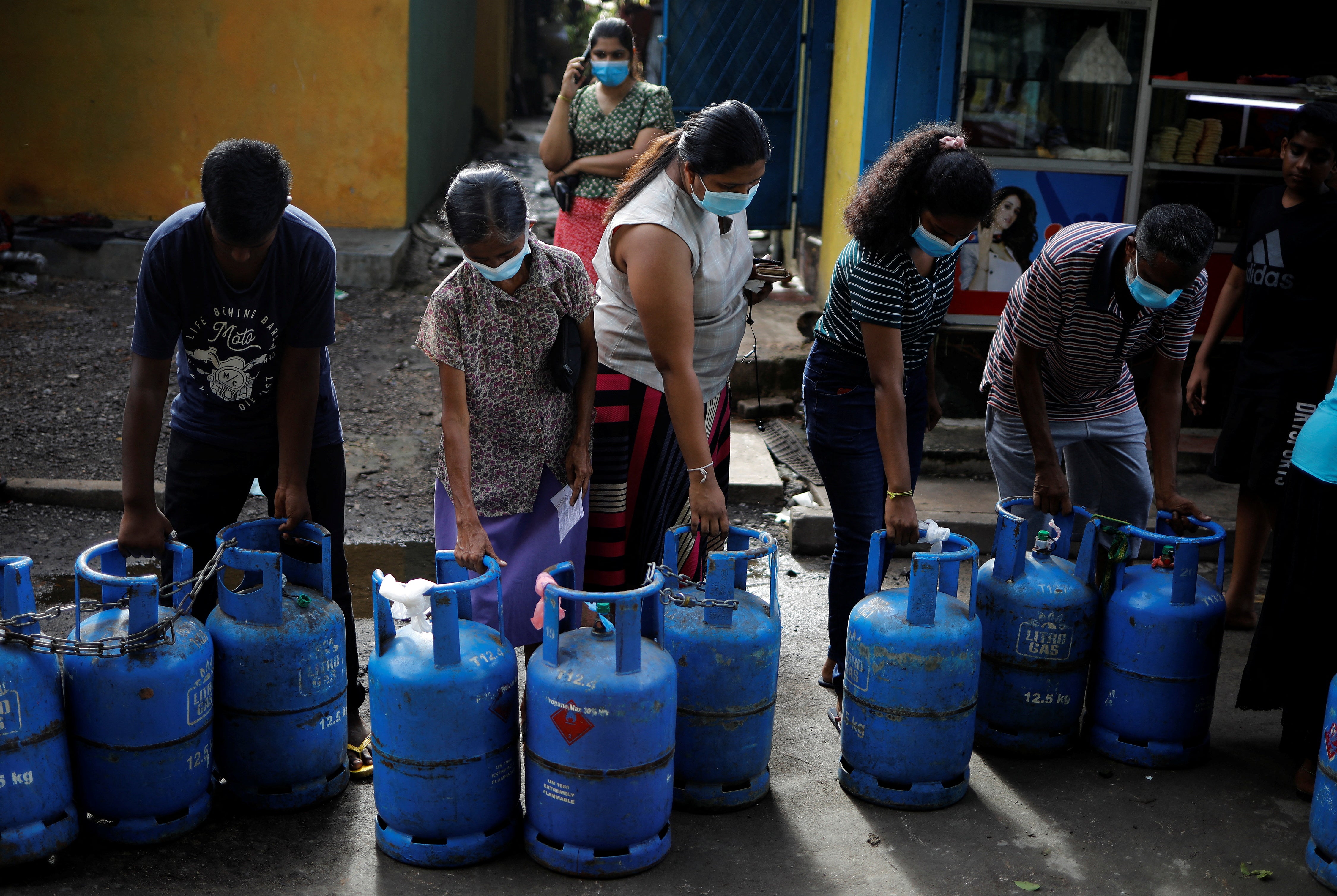 People carry their empty cylinders as they move in a queue to buy domestic gas at a distribution centre