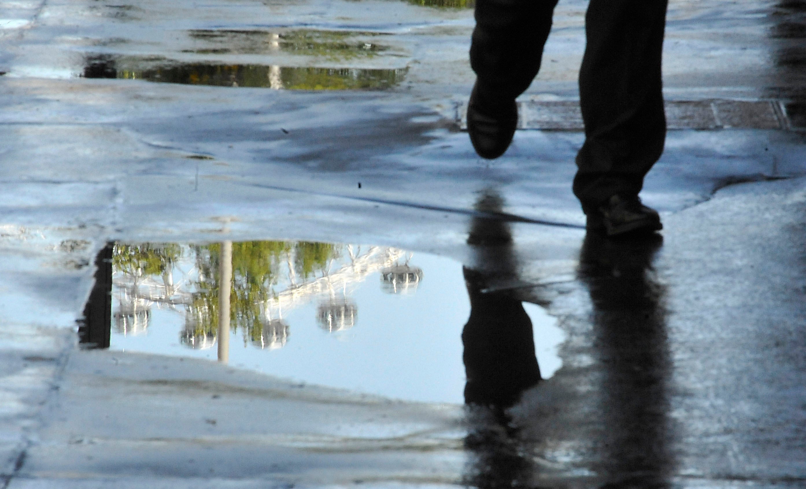 A man walks past a puddle reflecting the London Eye.