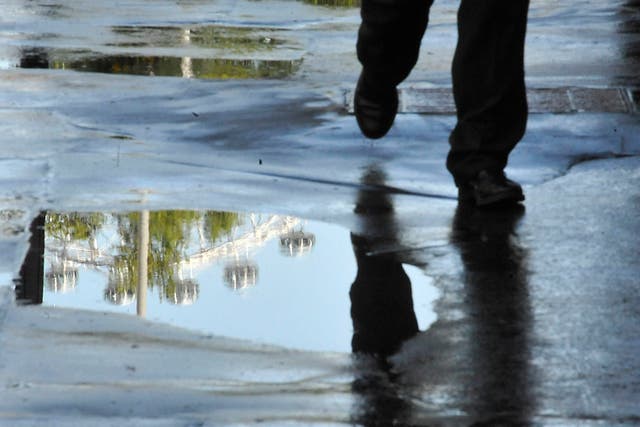 A man walks past a puddle reflecting the London Eye.