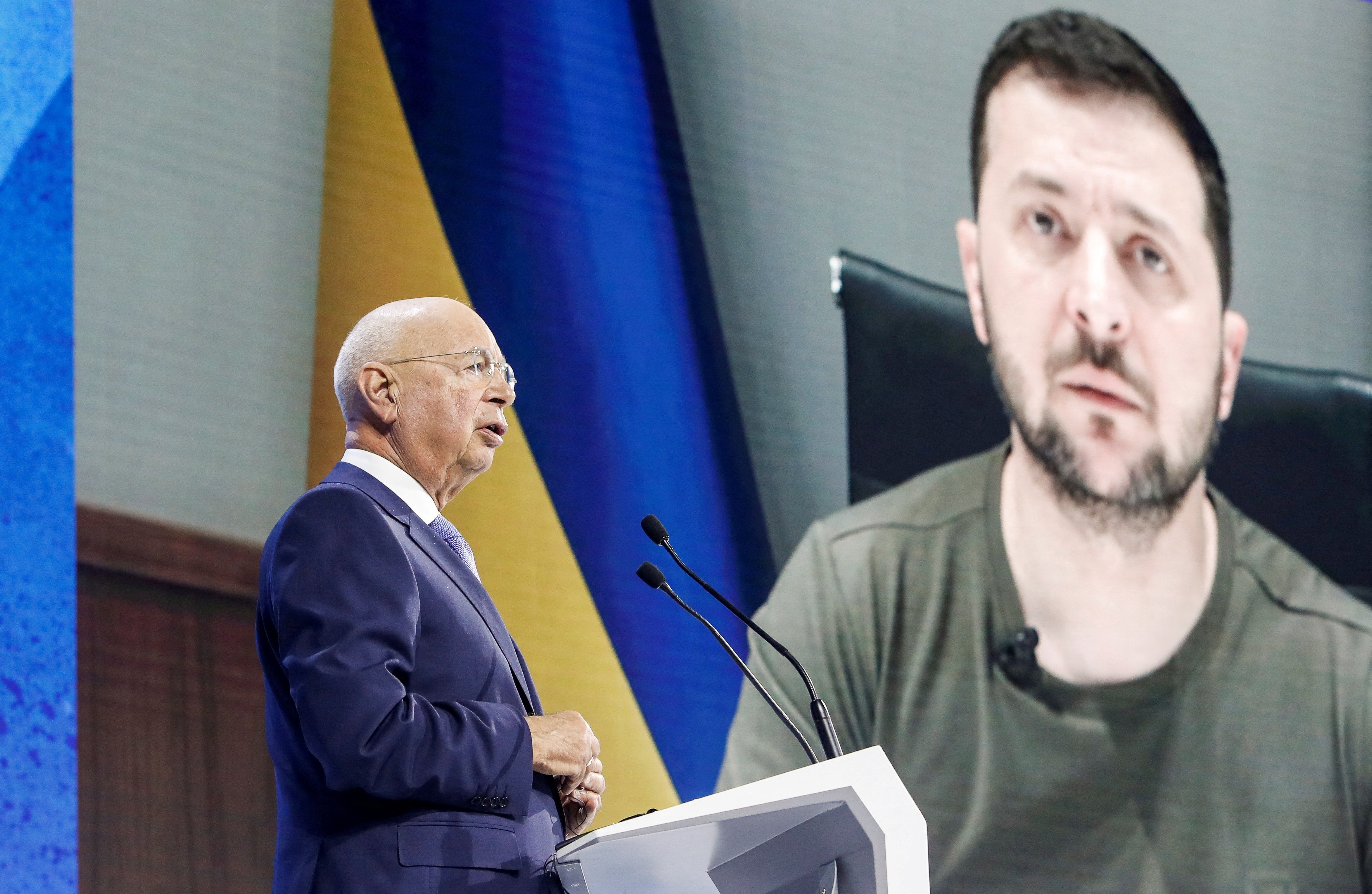 Founder and Executive chairman Klaus Schwab addresses the delegates with the Ukraine’s President Volodymyr Zelensky displayed on a screen in the background during the opening ceremony of the World Economic Forum (WEF) in Davos