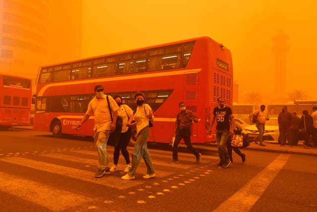 <p>People walk on a street shrouded in heavy dust in Kuwait City</p>