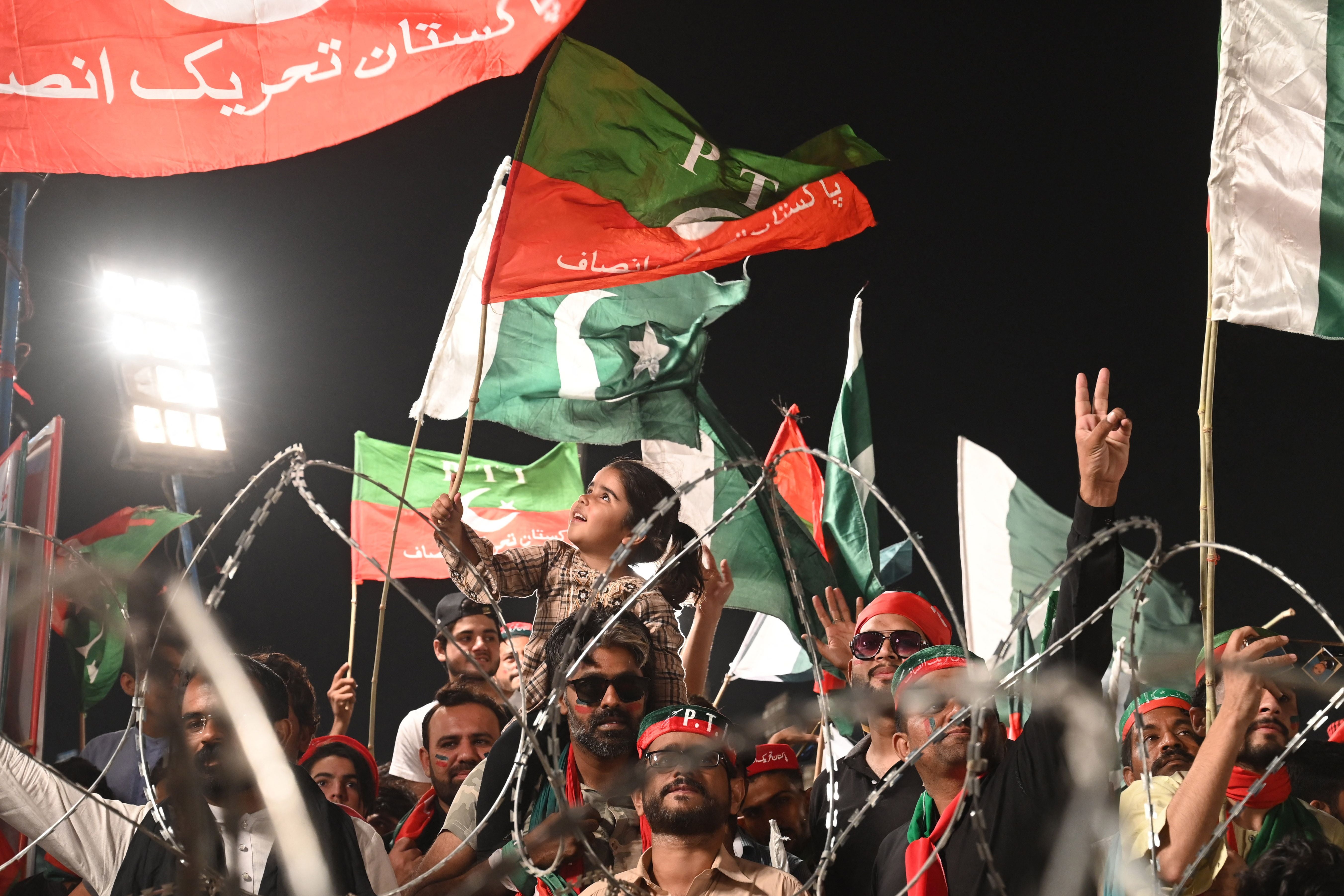 Supporters of Imran Khan’s Pakistan Tehreek-e-Insaf (PTI) party hold Pakistani and party flags as they listen to his speech during a rally in Lahore