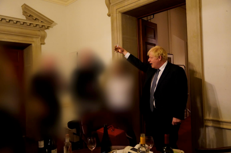 Holding up a plastic cup, Mr Johnson addresses the room