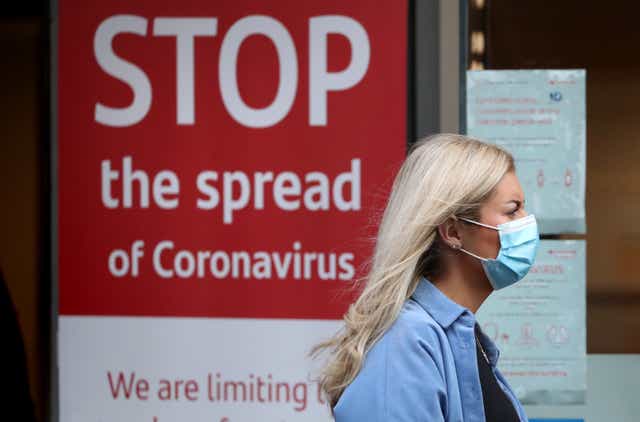 <p>A woman wearing a Covid mask passes a public health warning poster </p>