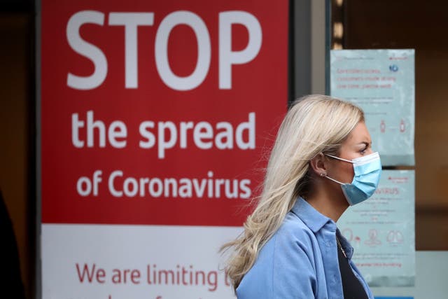 <p>A woman wearing a Covid mask passes a public health warning poster </p>