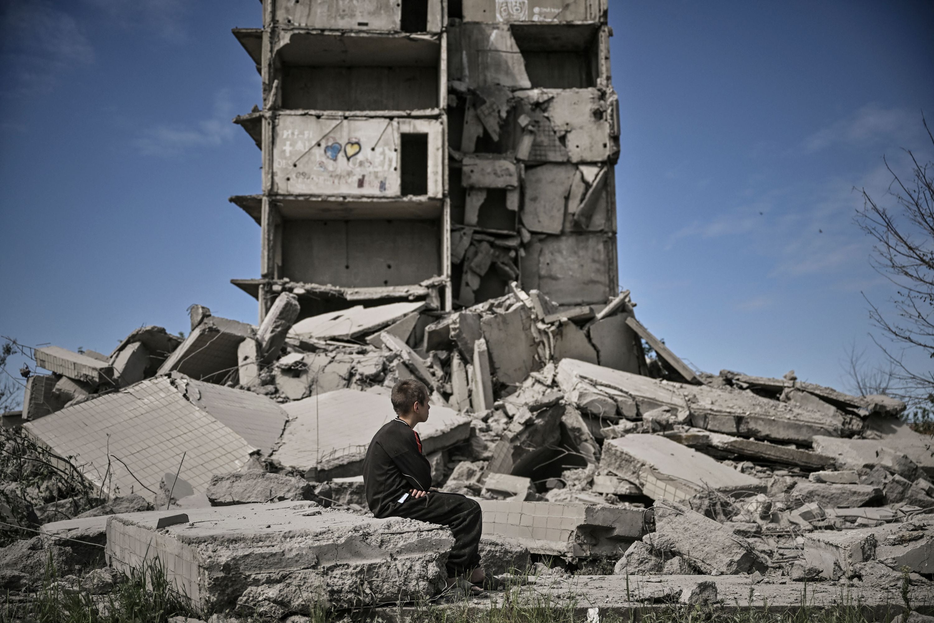 A young boy sits in front of a damaged building after a strike in Kramatorsk in the eastern Ukranian region of Donbas