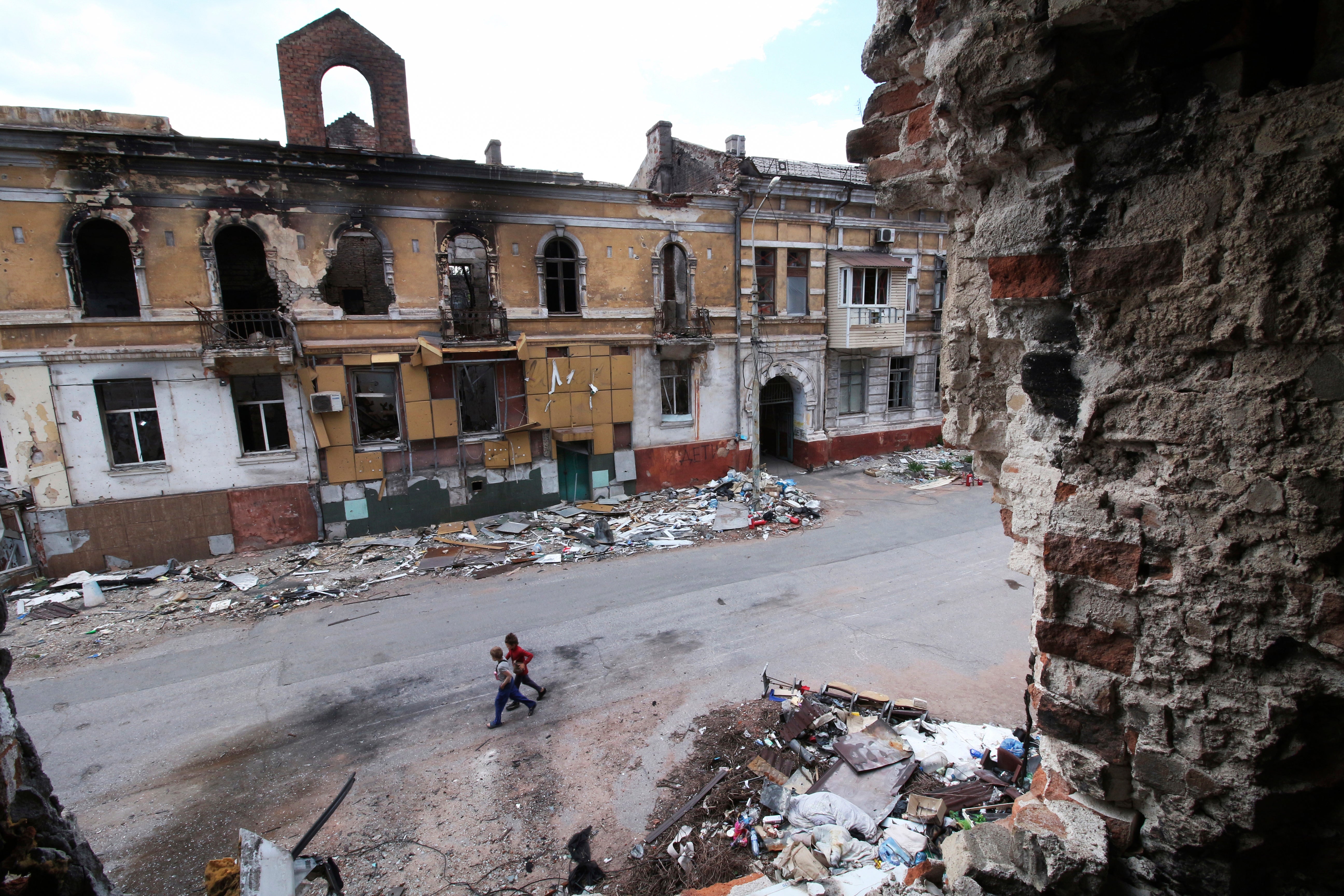 Children walk among destroyed buildings in Mariupol, which is now under Russian control