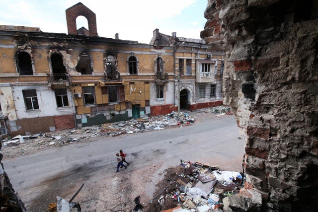 <p>Children walk among destroyed buildings in Mariupol, which is now under Russian control</p>