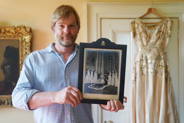 Rory Campbell holding a photograph of his mother Lady Moyra Campbell with Queen Elizabeth II on Coronation day, alongside the dress Lady Campbell wore (Brian Lawless/PA)
