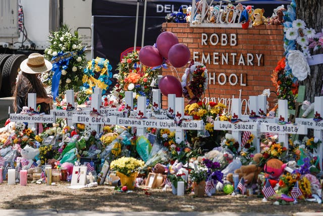 <p>A woman kneels amongst crosses bearing names of victims following the mass shooting at the Robb Elementary School</p>