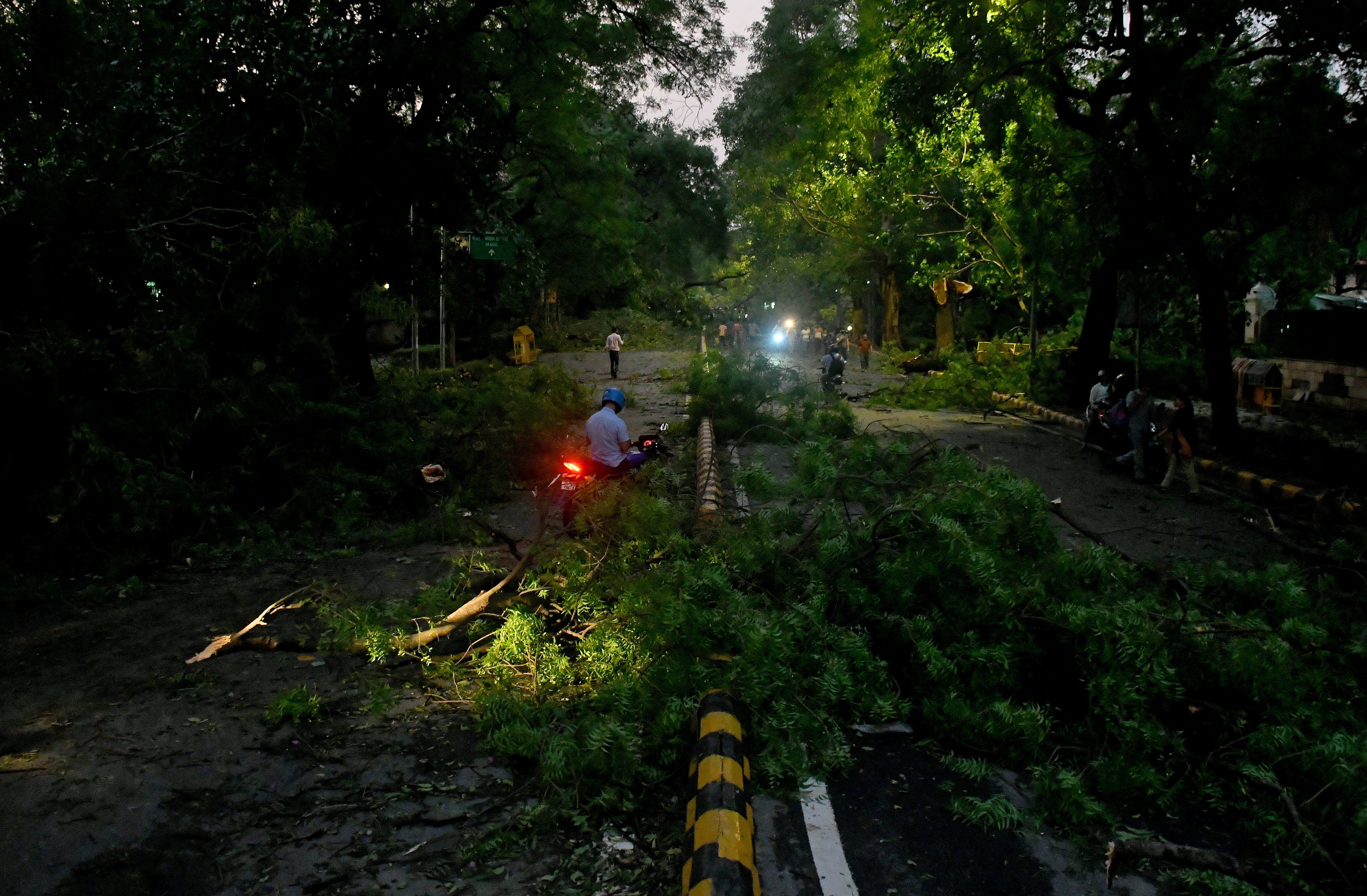 People move past fallen tree branches after heavy wind and rain in New Delhi