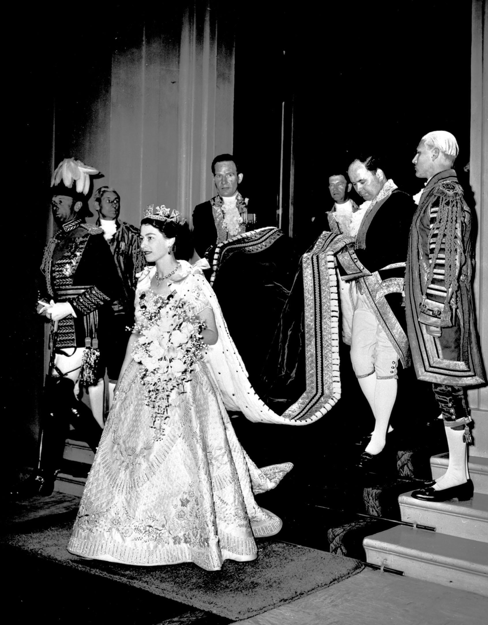 A footman lifts the Queen’s train as she leaves Buckingham Palace to enter the State Coach following her Coronation (PA)