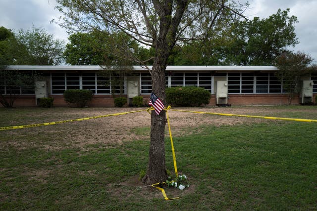 <p>A school building stands behind a tree with an American flag and crime scene tape at Robb Elementary School in Uvalde, Texas Monday, May 30, 2022</p>