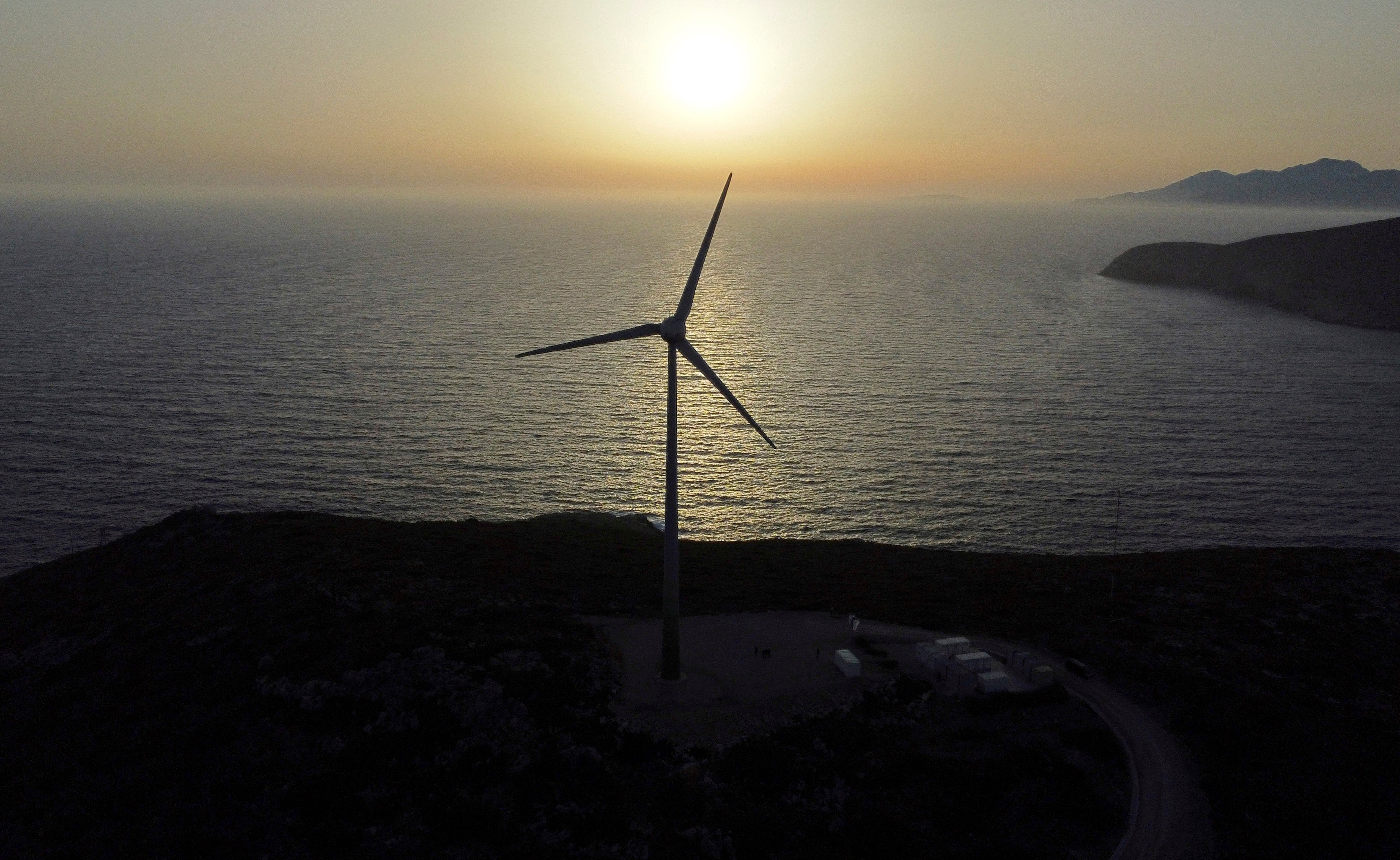 The sun sets behind a wind turbine
