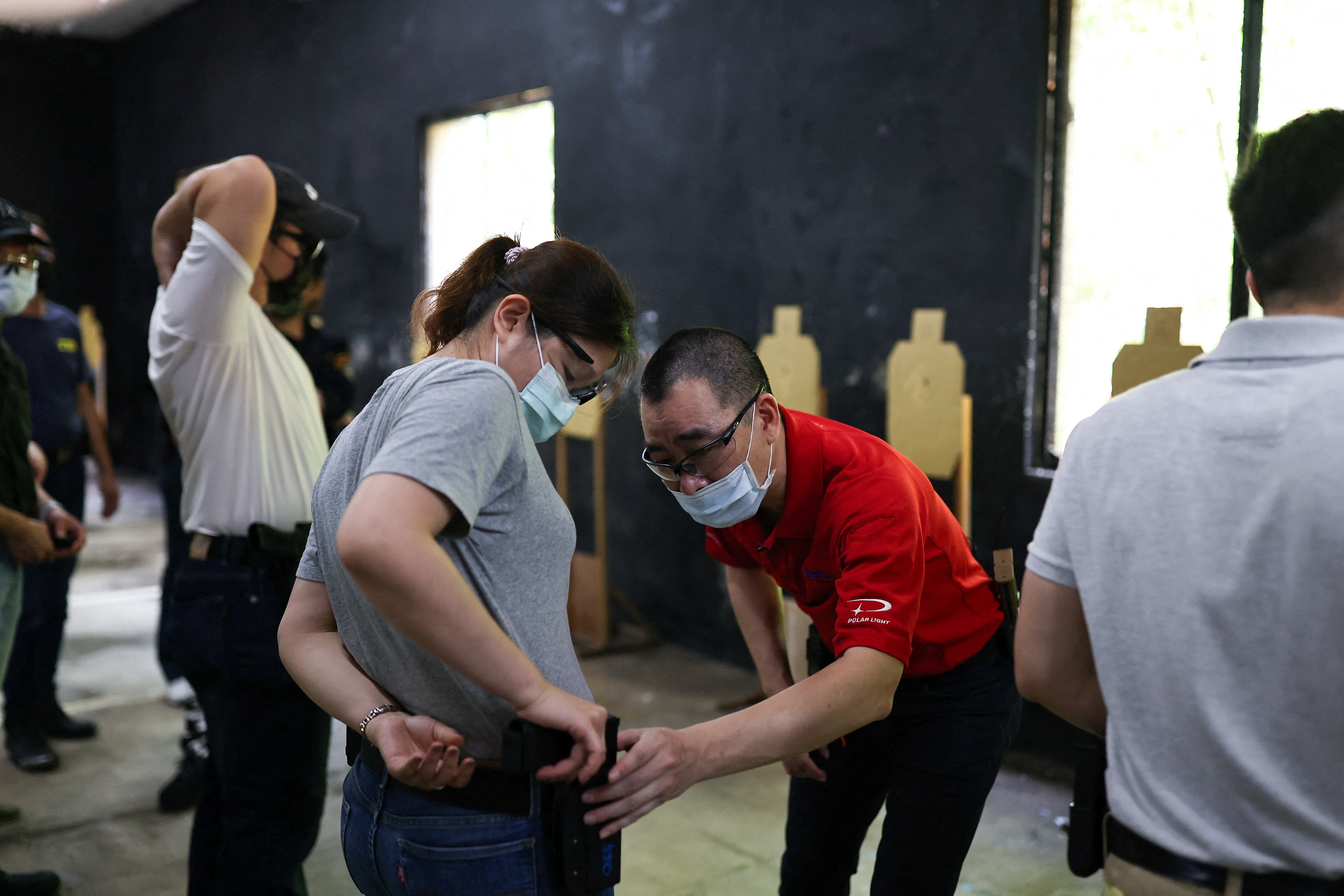 A trainer checks if a female trainee’s airsoft handgun is placed correctly in the holster during a basic training class