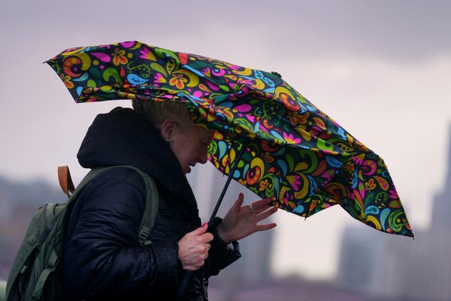 A woman struggles with an umbrella as she walks over Westminster Bridge during high winds and wet weather (Victoria Jones/PA)