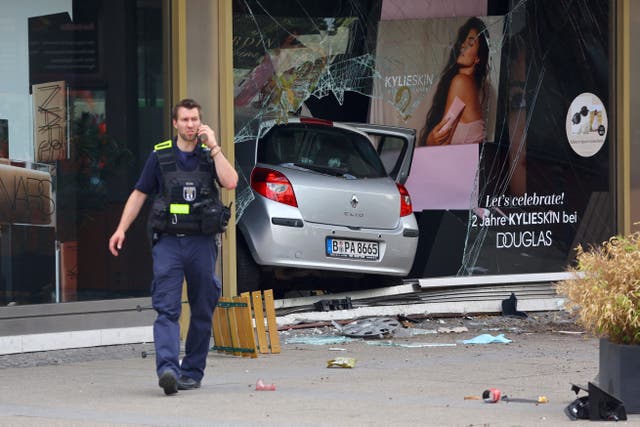 <p>A police officer speaks on the phone near the car at crashed into a group of people and ended up in a storefront</p>