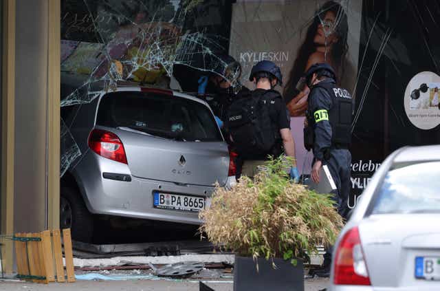 <p>Police investigators stand near a car that ploughed into pedestrians and then smashed into a perfume store on Tauentzienstrasse</p>