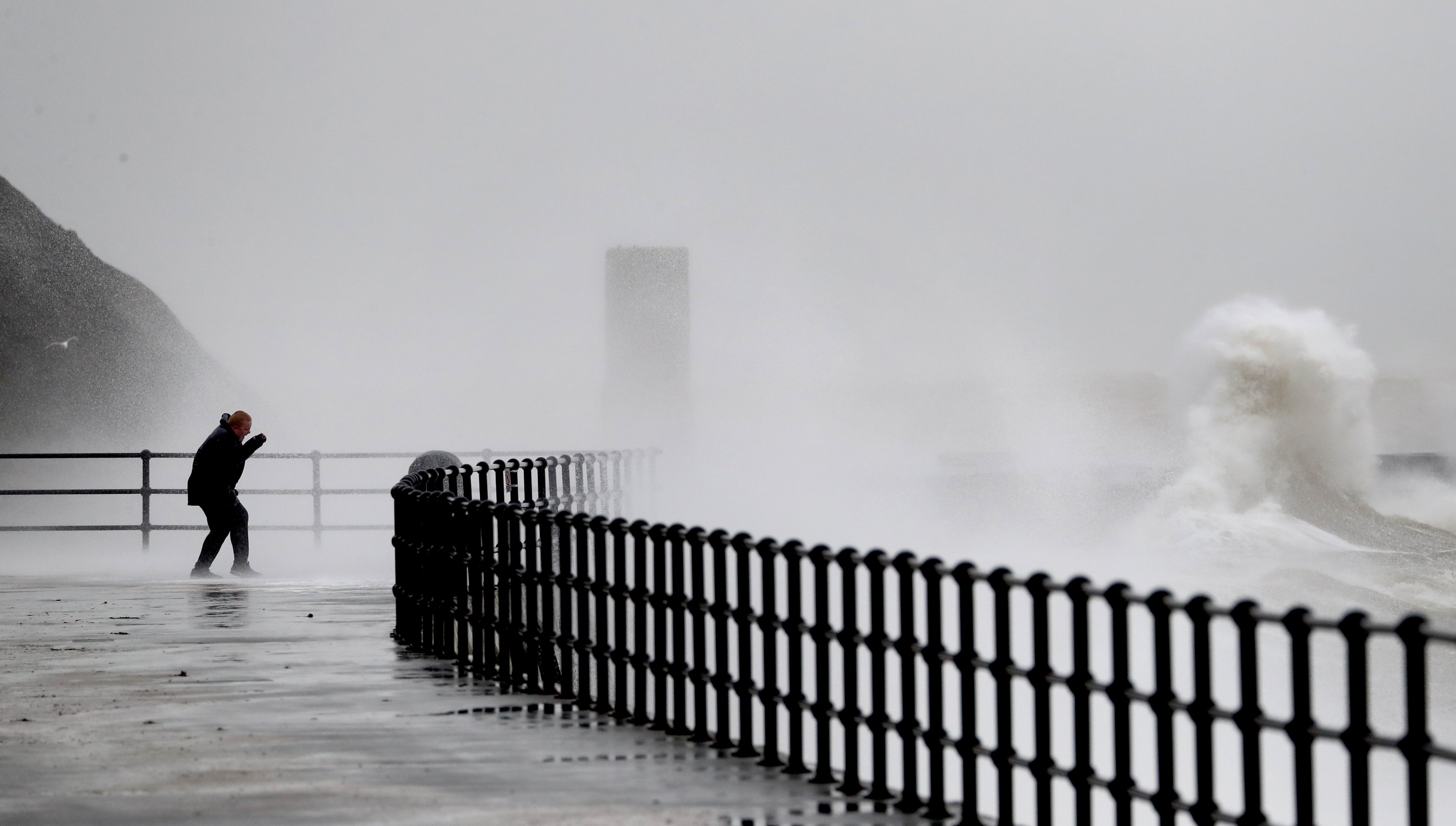 A man watches waves crashing over the promenade (Gareth Fuller/PA)