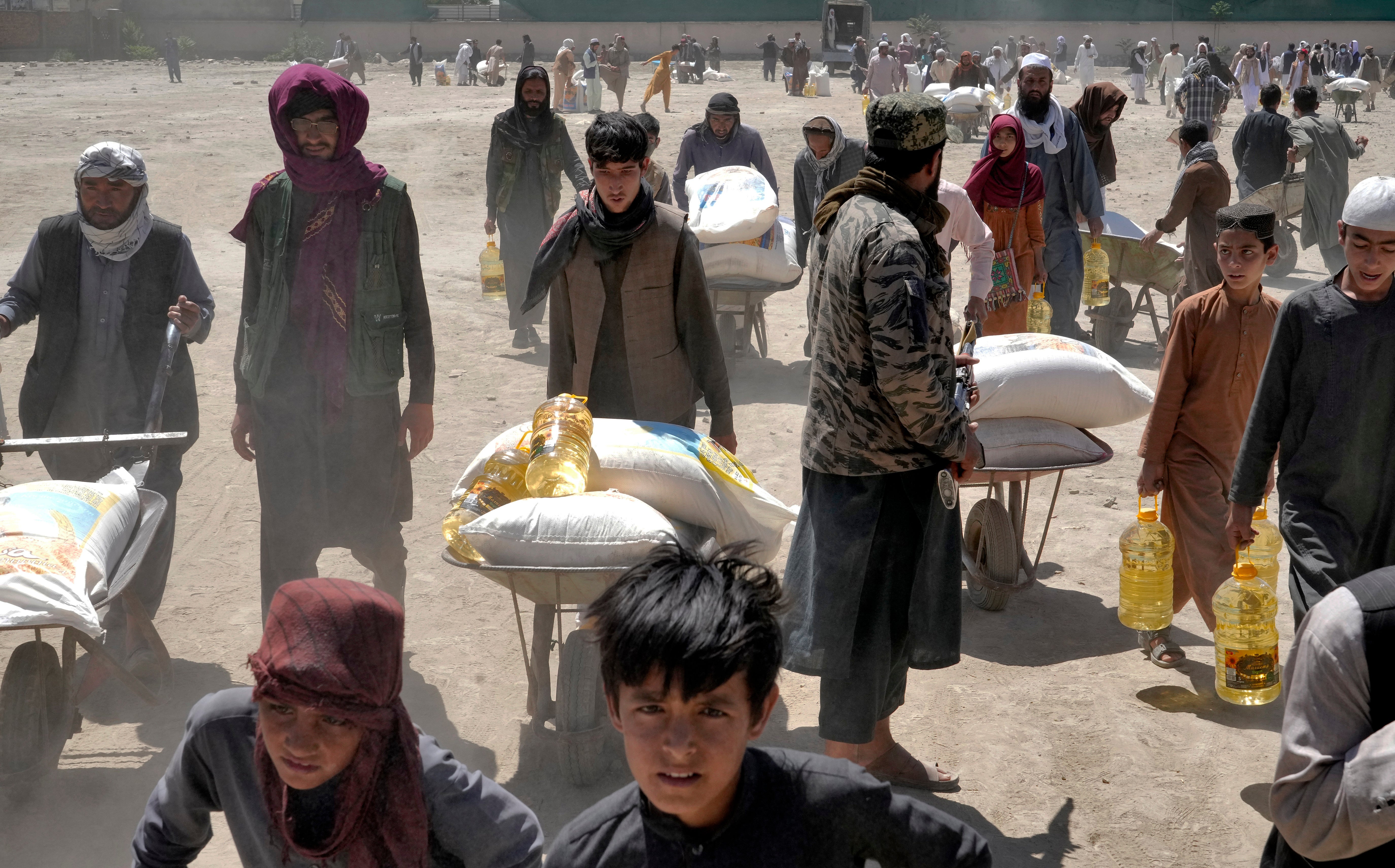 A Taliban fighter stands guard as people receive food rations distributed by a Chinese humanitarian aid group, in Kabul, Afghanistan, Saturday, 30 April 2022