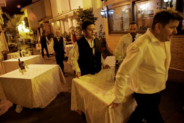 <p>Waiters move a table from a restaurant’s terrace as people are evacuated because of the forest fire</p>