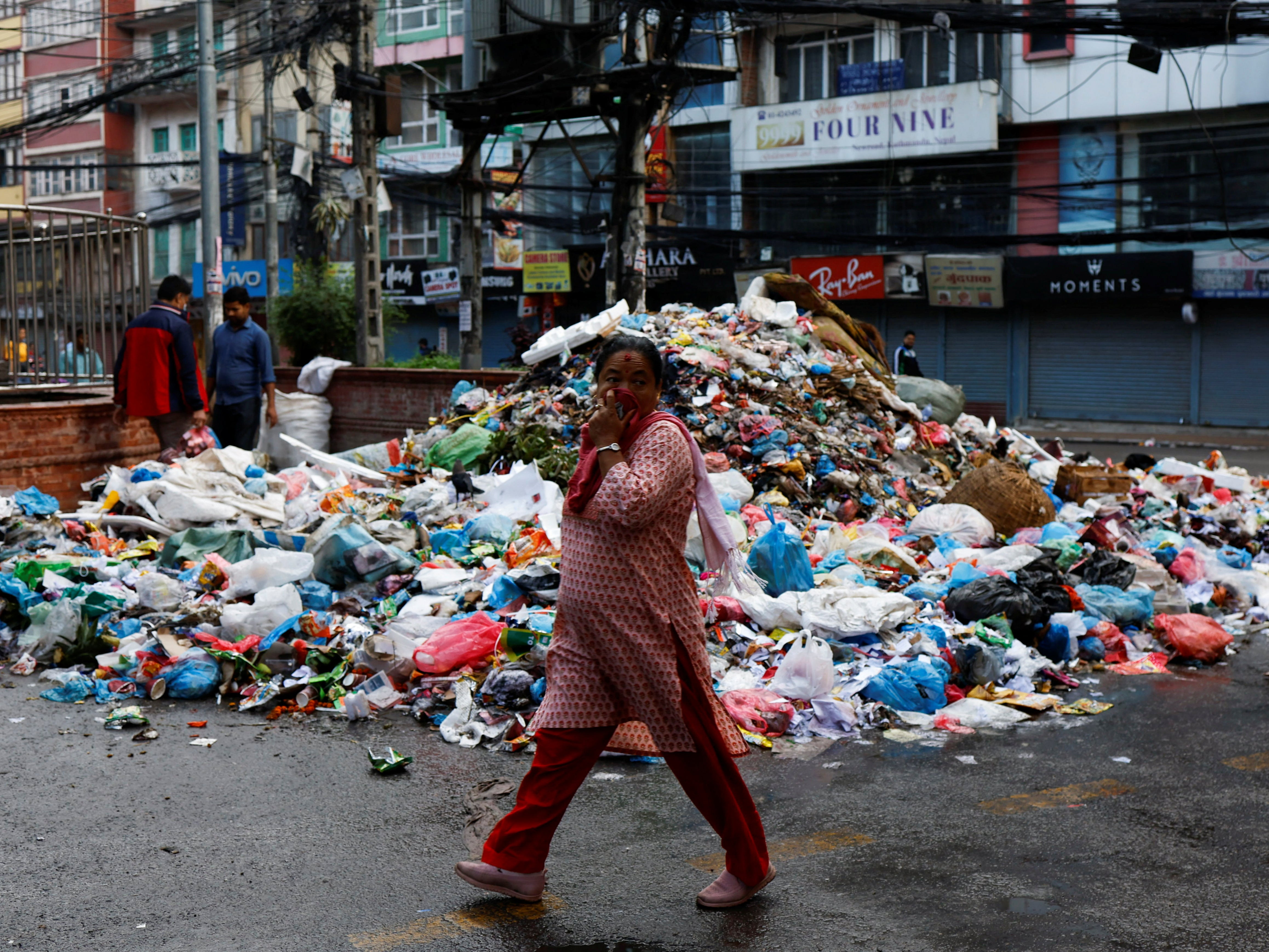 A woman covers her face as she walks past a pile of garbage dumped along the street in New Road in Kathmandu on 8 June