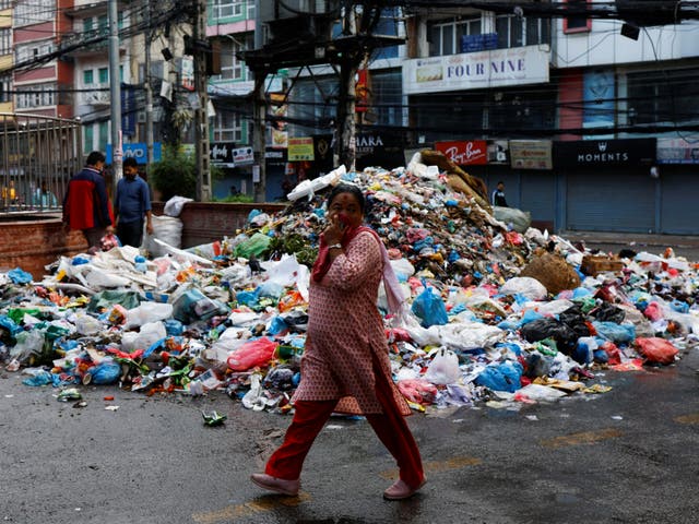 <p>A woman covers her face as she walks past a pile of garbage dumped along the street in New Road in Kathmandu on 8 June</p>