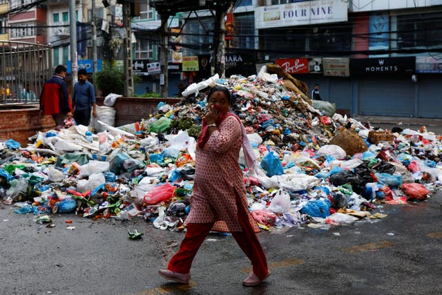 <p>A woman covers her face as she walks past a pile of garbage dumped along the street in New Road in Kathmandu on 8 June</p>