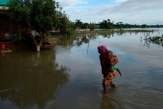 <p>A woman holding a child walks through flooded waters in Sunamganj, Bangladesh on July 14, 2020</p>