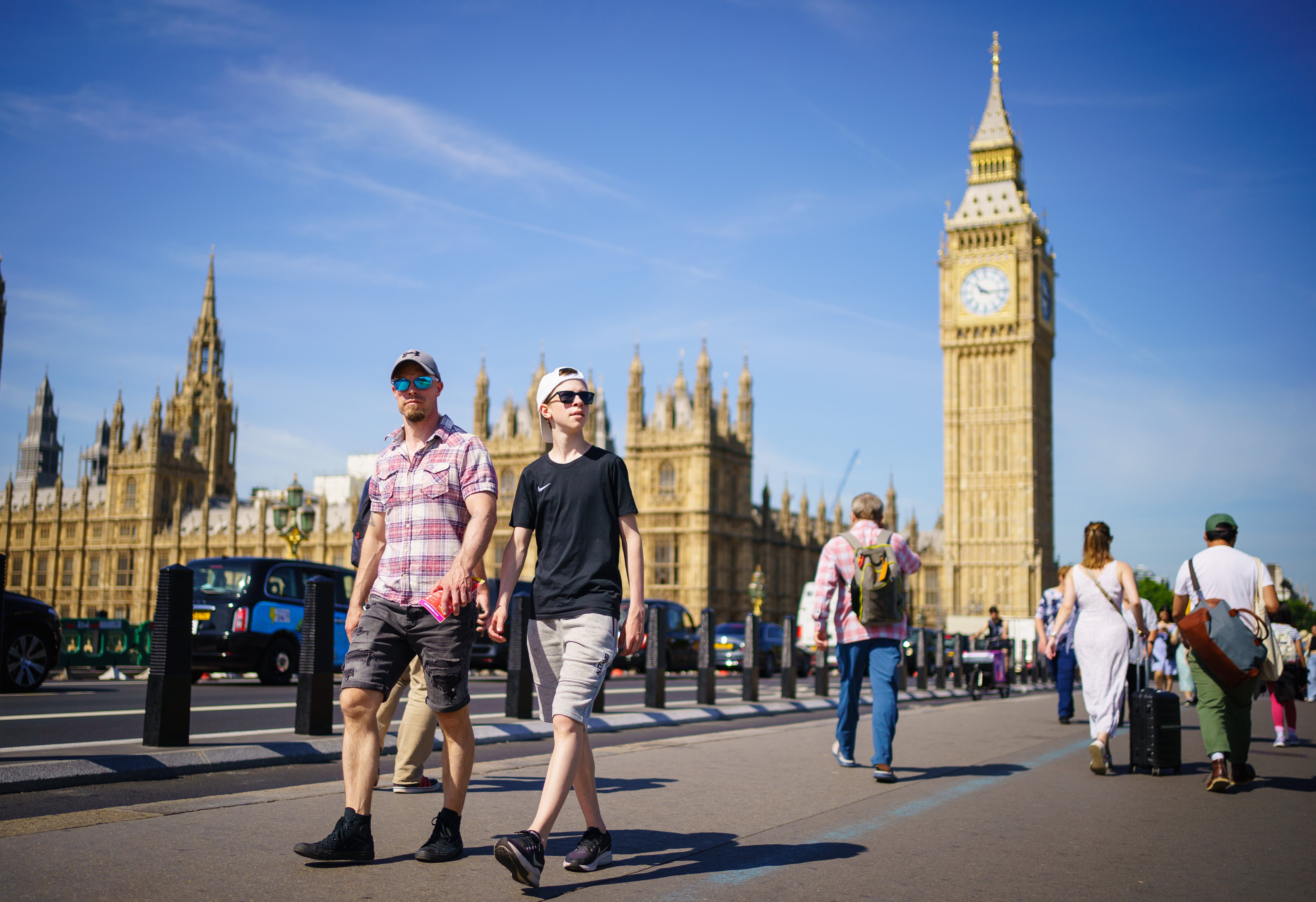People enjoy the sunny weather on Westminster Bridge, by the Houses of Parliament, London