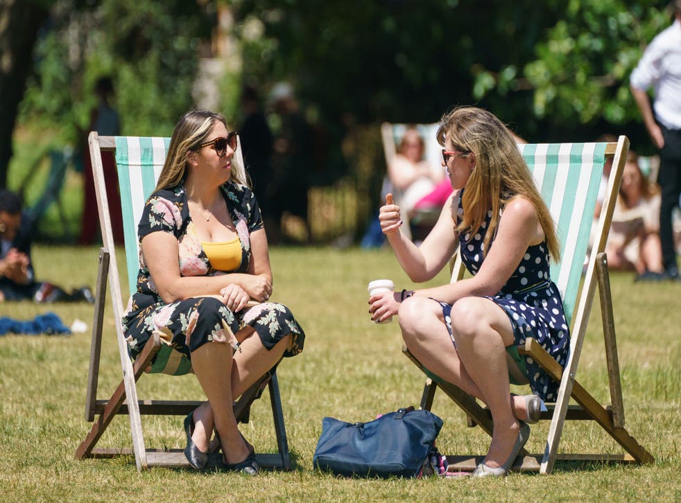 Two women sit in deck chairs as people enjoy the warm weather in Green Park, London (PA)