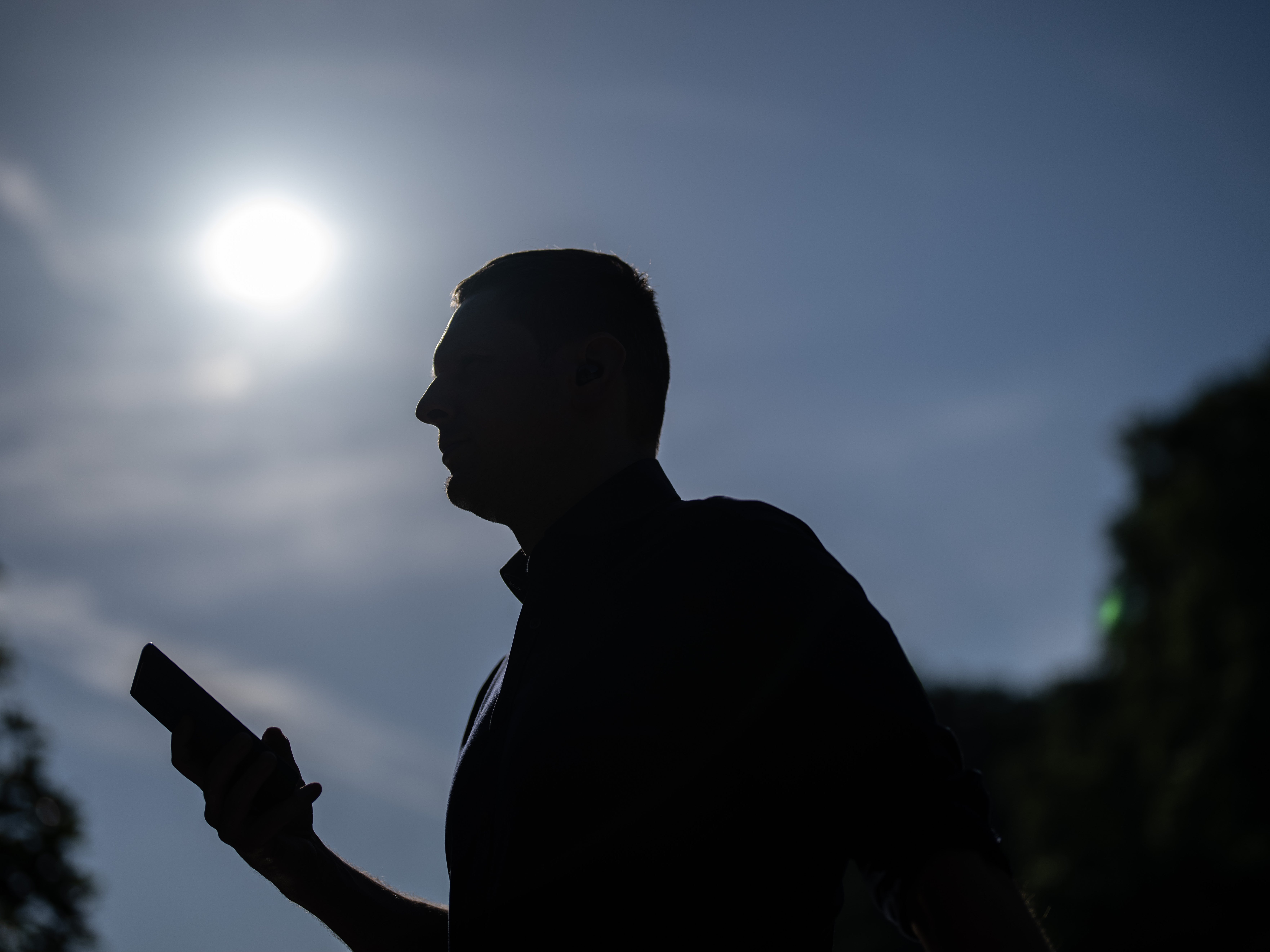 A man checks his phone as he walks through the heat in St James’s Park, London