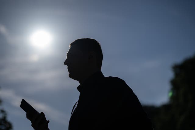 <p>A man checks his phone as he walks through the heat in St James’s Park, London</p>