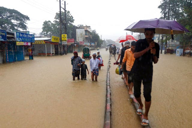 <p>People wade along a road in a flooded area following heavy monsoon rainfall in the city of Sylhet in Bangladesh on 18 June</p>