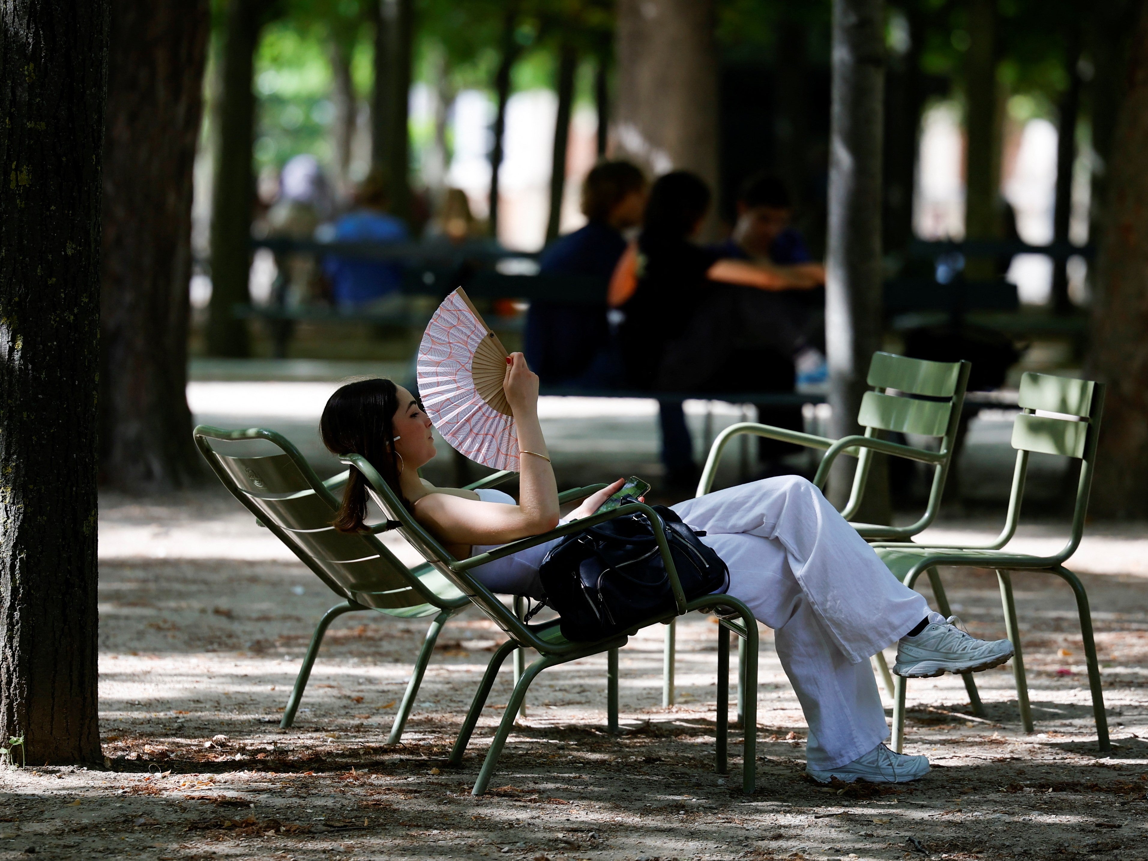 A woman uses a fan to cool down at the Luxembourg Gardens in Paris as an early heatwave hits the country