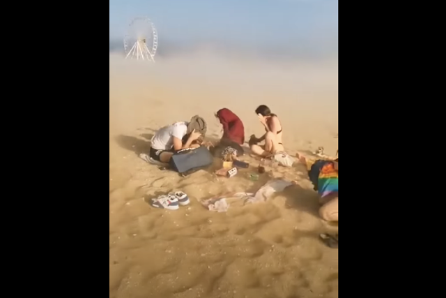 <p>Screengrab from a video that shows beach-goers in France’s Villers-sur-Mer covering their faces with towels to shield them from the dust and sand</p>