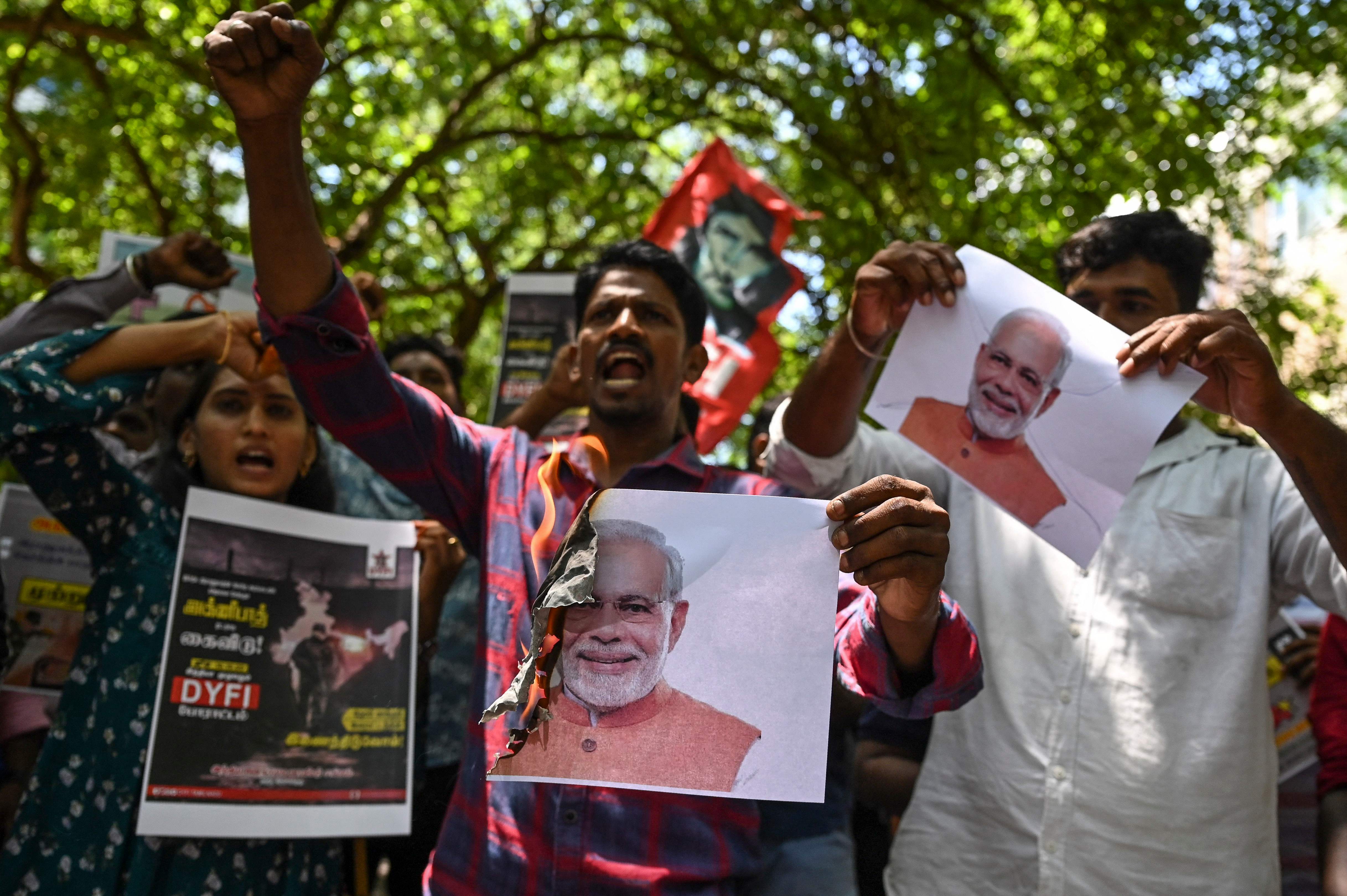 Protesters shout slogans and burn placards with pictures of Prime Minister Modi