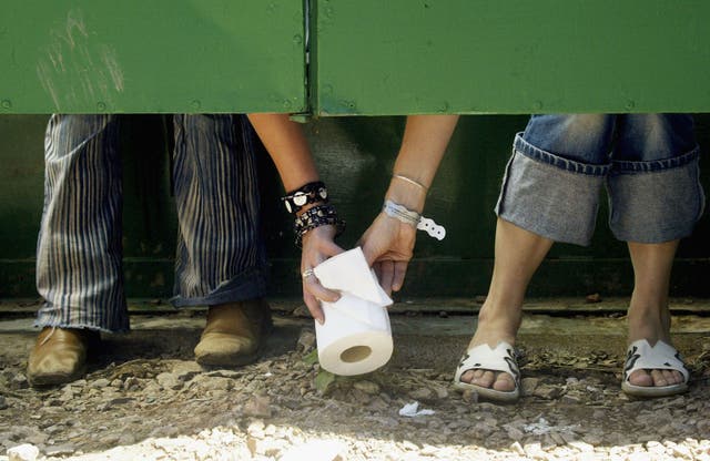 <p>Two festival-goers pass a roll of toilet paper between toilet cubicles </p>