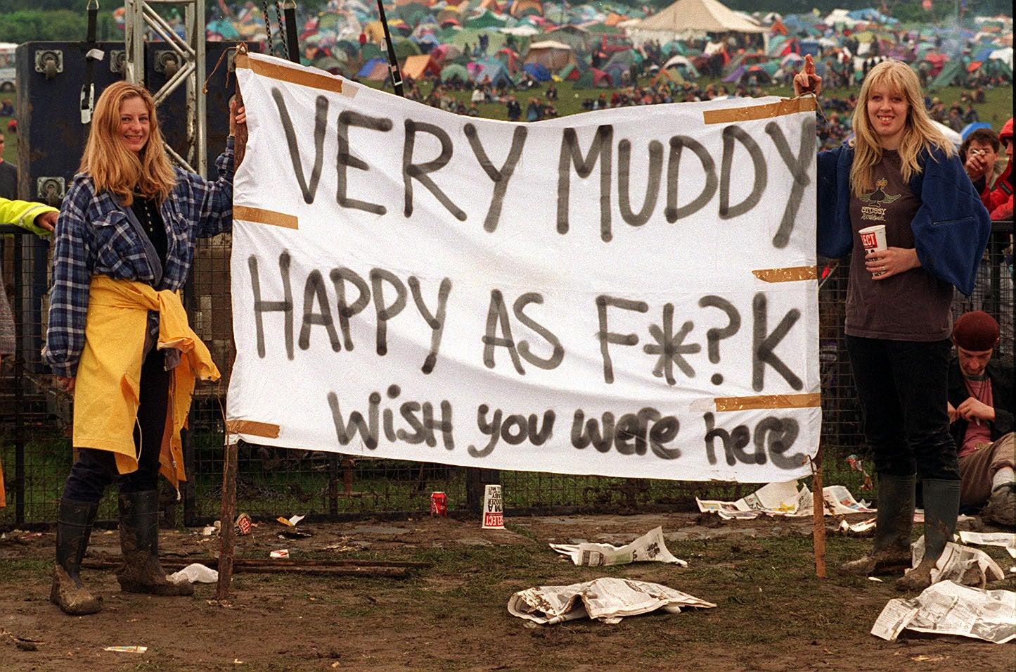 Music fans make the best of muddy conditions as they display a wish you were here banner in 1997