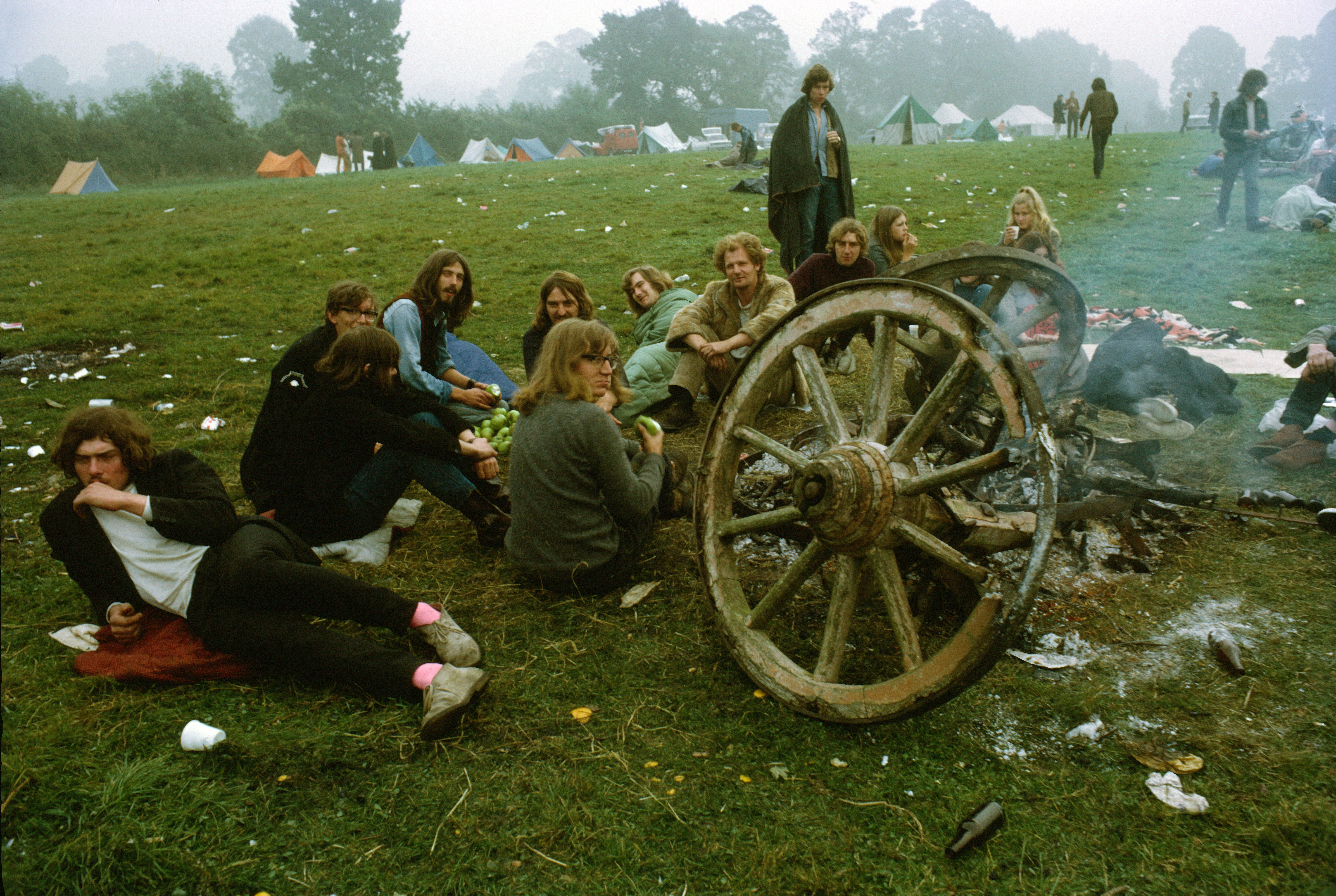 A group eating apples next to a smouldering wooden cart at the first Glastonbury Festival, 1970
