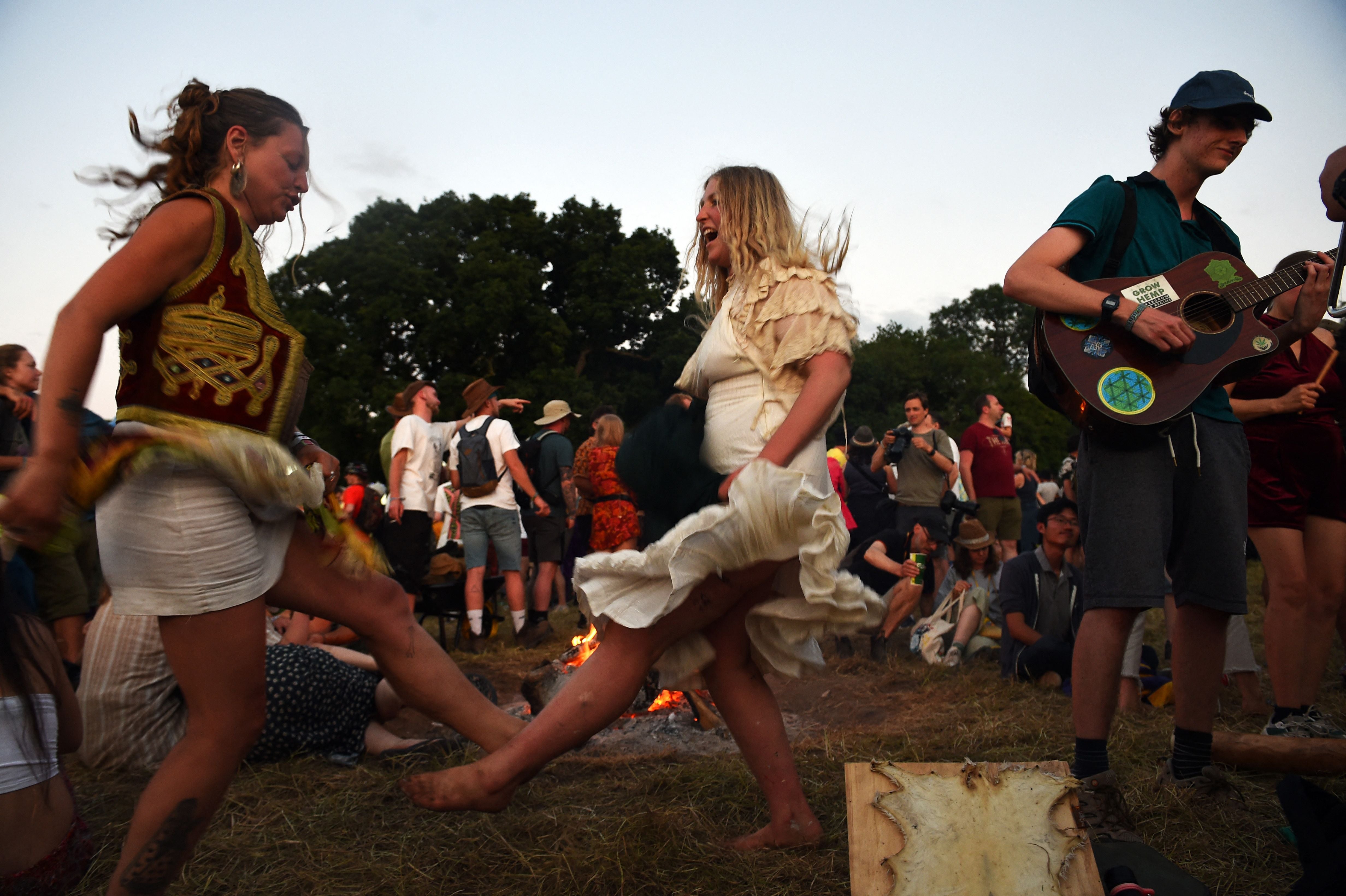 A festivalgoer plays the guitar as others dance around a bonfire