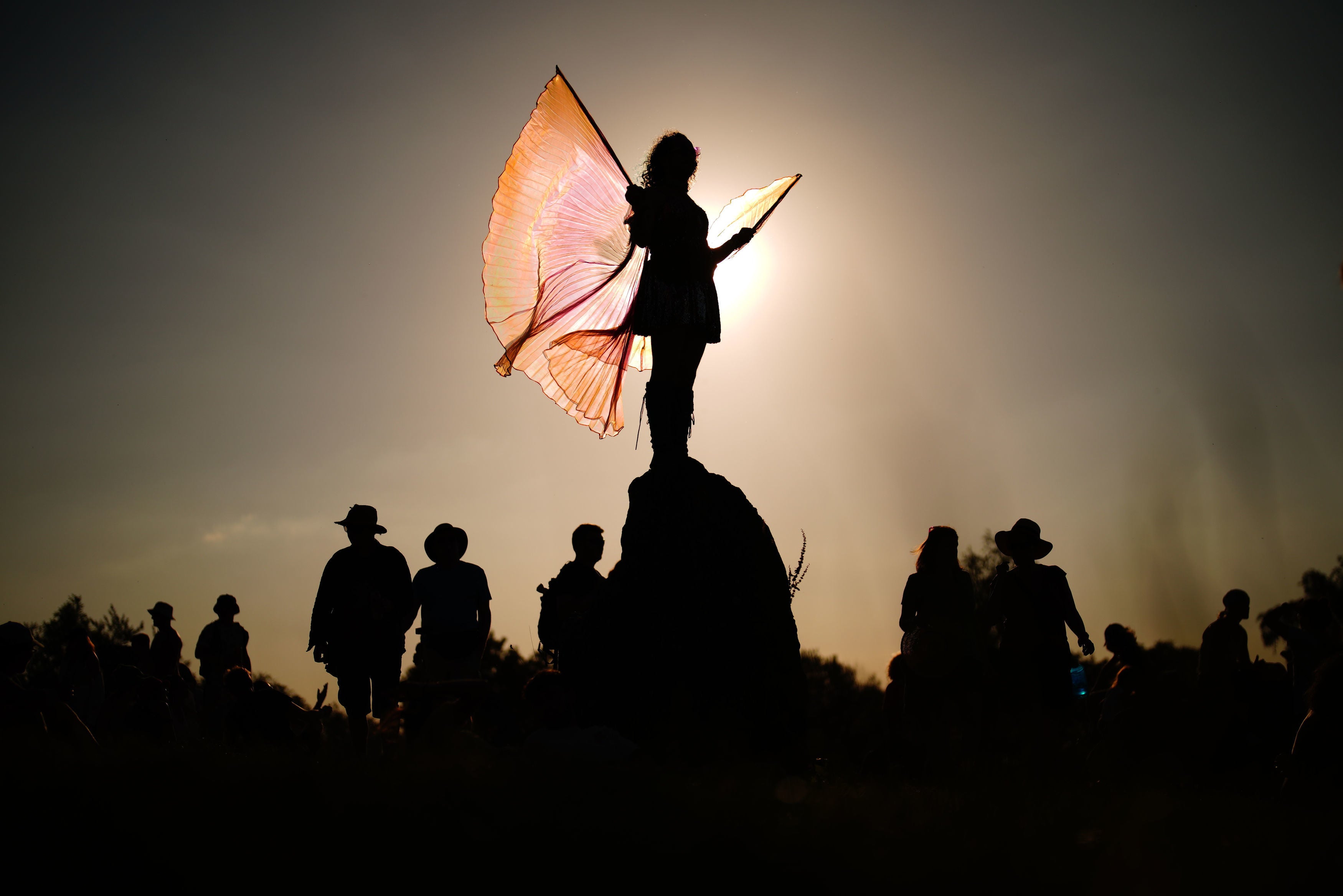 A festival attendee is silhouetted as they stand atop of the stone circle