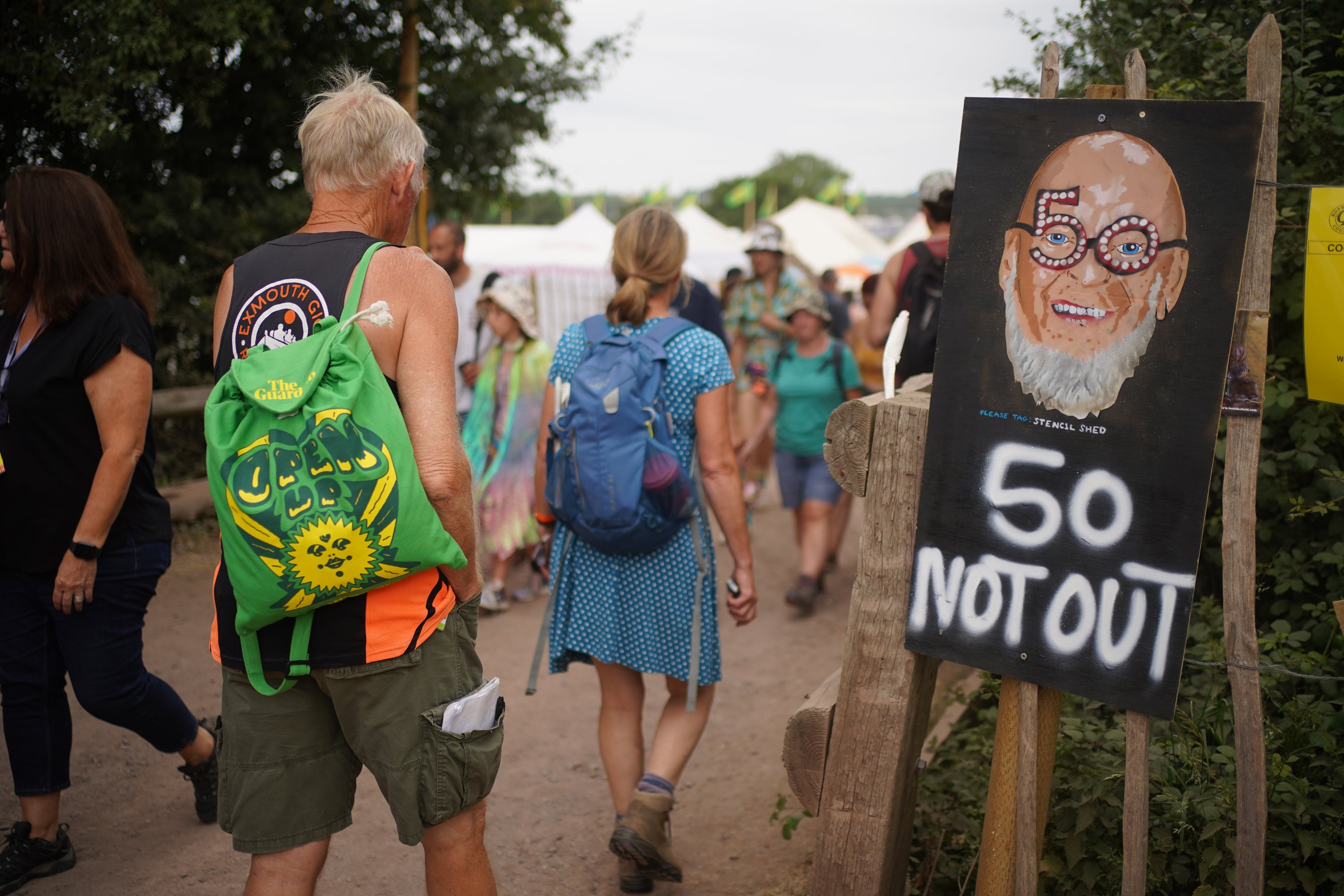 Festival-goers walk past a Michael Eavis sign (Yui Mok/PA)