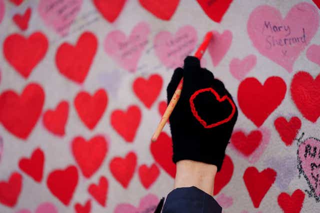A volunteer from the Covid-19 Bereaved Families for Justice campaign group paints a heart on the National Covid Memorial Wall opposite the Palace of Westminster in central London, which remembers people who have died of the virus. (Victoria Jones/PA)