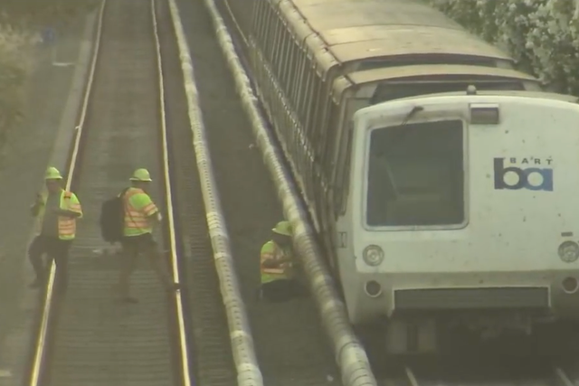 <p>Workers next to a BART train that partially derailed last week </p>