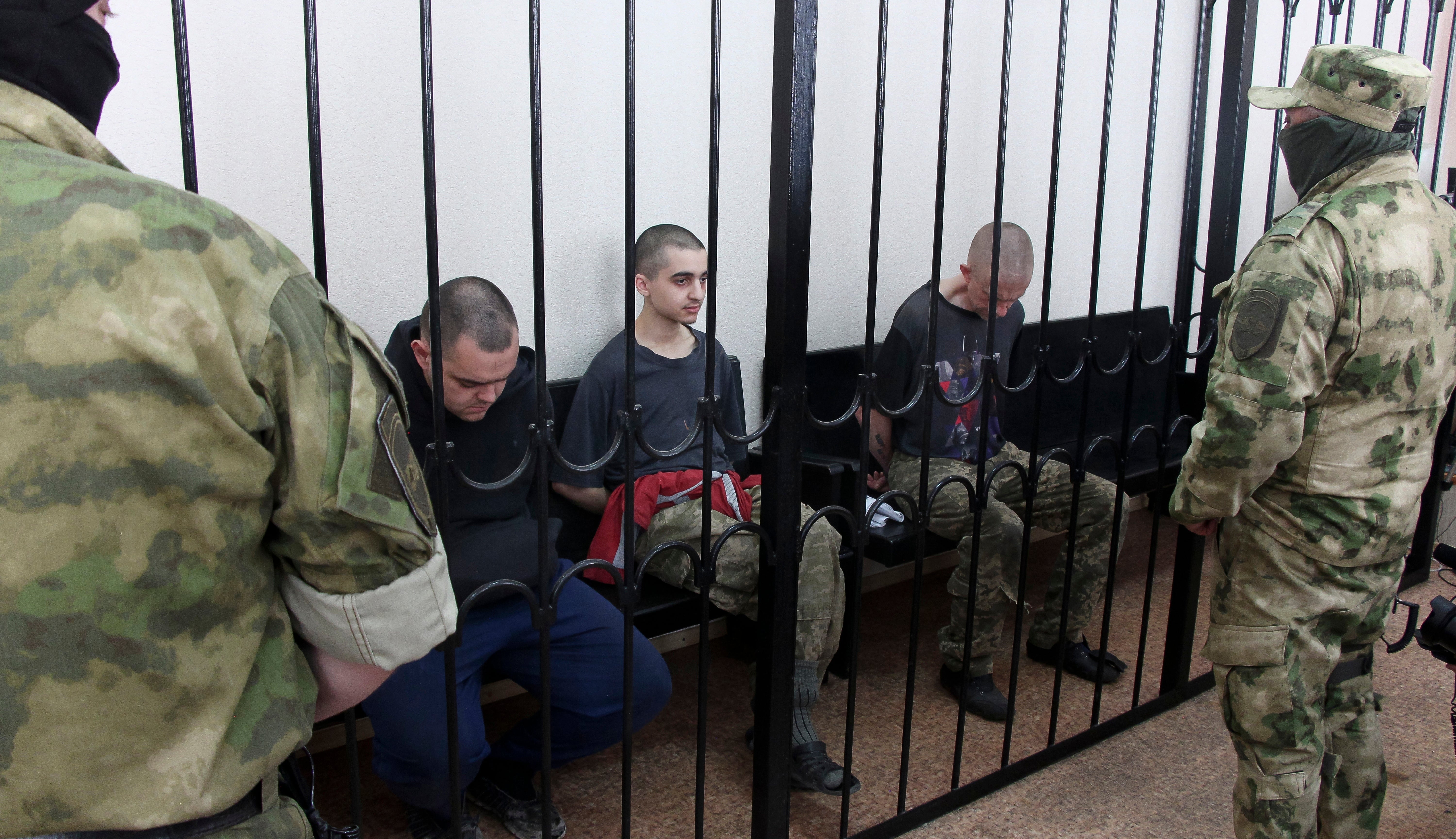 Two British citizens Aiden Aslin, left, and Shaun Pinner, right, and Moroccan Saaudun Brahim, center, sit behind bars in a courtroom in Donetsk