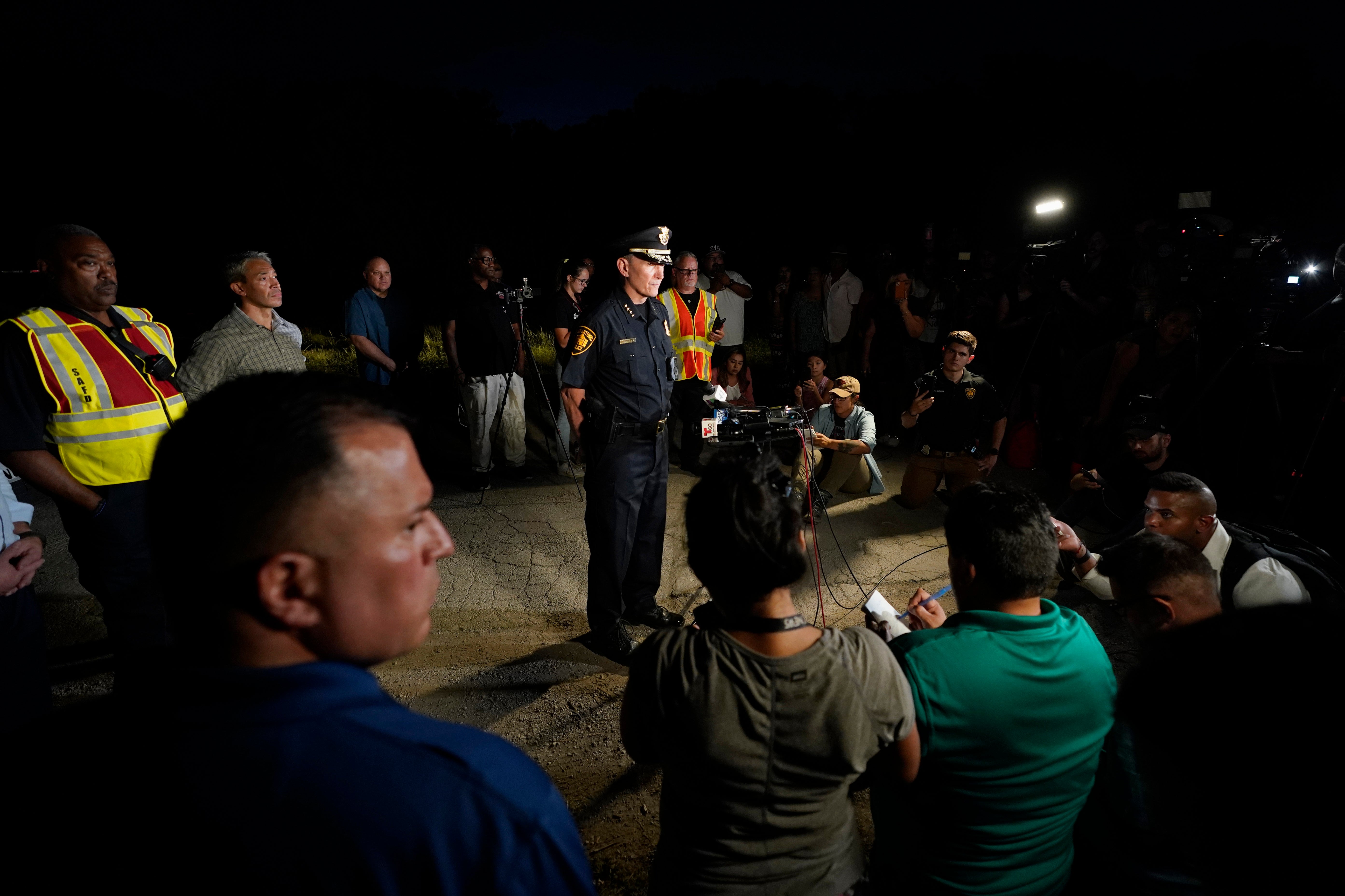 San Antonio Police Chief William McManus, center, briefs media and others at the scene where dozens of people were found dead and multiple others were taken to hospitals with heat-related illnesses after a semitrailer containing suspected migrants was found, Monday, June 27, 2022, in San Antonio