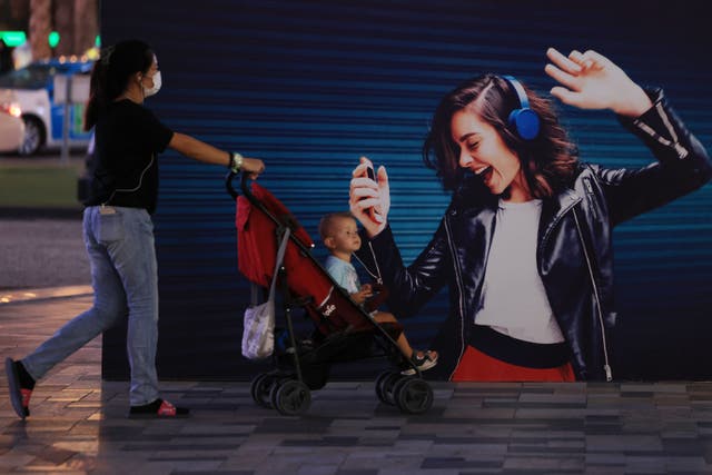 <p>A woman pushes a baby cart past a poster of a woman in headphones dancing displayed on a wall at Dubai’s Jumeirah Beach Residence on 16 November 2020</p>